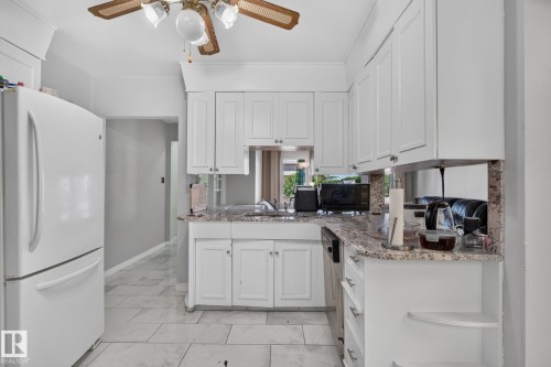Kitchen featuring white shaker-style cabinetry, granite-look countertops, tiled flooring, and a ceiling fan with integrated lighting - 12238 48 Street, Edmonton, AB 