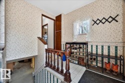 Entryway featuring wood balusters, a window with white curtains, patterned wallpaper, and tile flooring - 