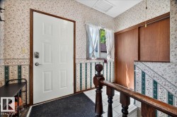 Entryway featuring a white paneled door with wood-finish trim, a window with sheer curtains, wood-finish sliding closet doors, and staircase with wood balusters - 