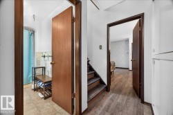 Hallway featuring wood-finish flooring, white painted walls, and dark wood trim - 