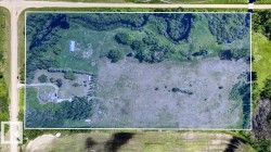 Aerial overview of a rectangular parcel featuring a residence, outbuilding, and varied terrain with wooded areas and open fields - 