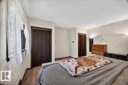 Bedroom featuring two dark wood-finish bifold doors, textured wallpaper, wood-finish flooring, and white ceiling - 