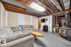 Basement space featuring exposed ceiling joists, concrete flooring, and a wood-burning stove with a chimney flue - 
