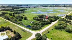 Rural property featuring a single-story residence surrounded by mature trees, multiple outbuildings, and expansive green spaces - 