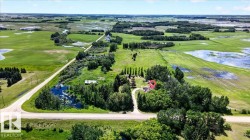 Expansive rural property featuring a winding driveway, mature tree coverage, a main residence, and additional outbuildings amidst vast open fields and natural water features - 