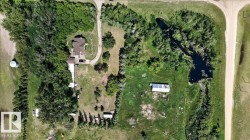 Aerial property overview featuring a main residence with a circular drive, several accessory structures, a large pond, and extensive tree coverage across the grounds - 