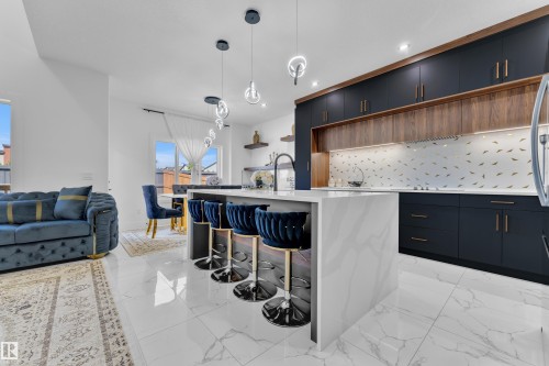 Gourmet kitchen featuring a waterfall island with a quartz countertop, custom dark cabinetry, wood-finish accent cabinetry, decorative backsplash, and integrated lighting - 16816 49 Street, Edmonton, AB 
