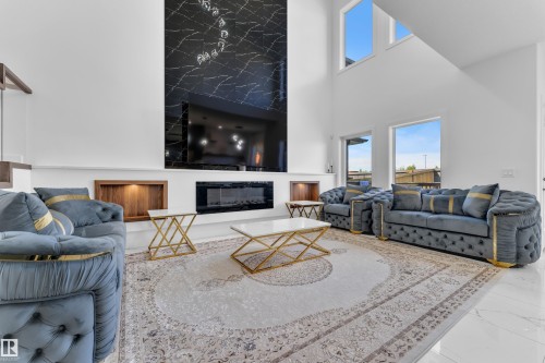 Spacious living area featuring a two-story ceiling, multiple windows, a stone-finish fireplace, and built-in shelving with accent lighting - 16816 49 Street, Edmonton, AB 