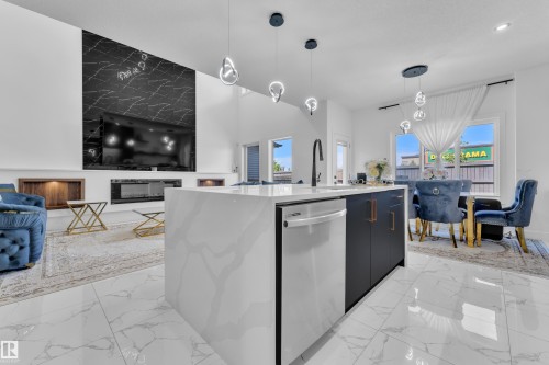 Spacious open-concept living area featuring large format white marble-look flooring, a kitchen island with a waterfall countertop, and a built-in electric fireplace - 16816 49 Street, Edmonton, AB 