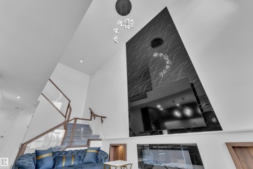 Vaulted ceiling living area featuring a dramatic black and white veined accent wall, a contemporary linear fireplace, and a striking glass and wood-finish staircase - 16816 49 Street, Edmonton, AB 