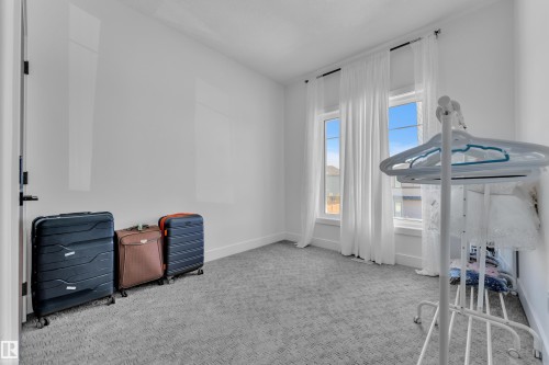 Bright interior space featuring two tall windows with sheer white drapery, white walls, and gray patterned carpet - 16816 49 Street, Edmonton, AB 