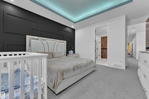 Spacious room featuring a tray ceiling with integrated lighting, a paneled accent wall, recessed lighting, and soft grey carpeting - 16816 49 Street, Edmonton, AB 