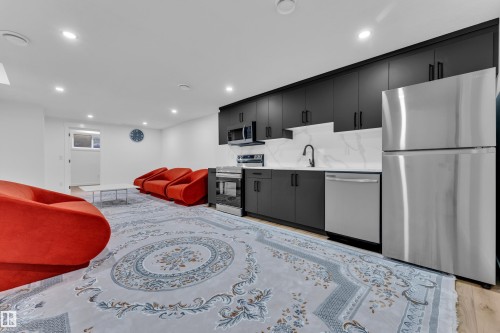 Modern kitchen space featuring matte black cabinetry, stainless steel appliances, and a marble-patterned backsplash - 16816 49 Street, Edmonton, AB 