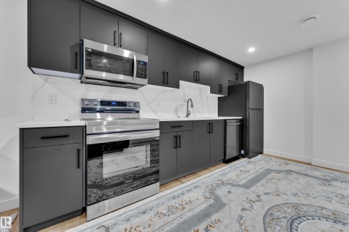 Modern kitchen featuring matte black cabinetry, stainless steel appliances, white countertops, and a white marble-patterned backsplash - 16816 49 Street, Edmonton, AB 