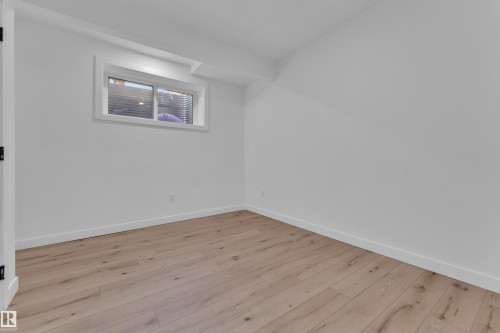 Bright room featuring wood-finish flooring, white painted walls, crisp white baseboards, and a window with horizontal blinds - 16816 49 Street, Edmonton, AB 