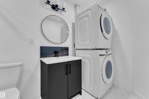 Compact laundry area featuring a stacked washer and dryer, a black vanity with white countertop, a round mirror, and patterned backsplash - 16816 49 Street, Edmonton, AB 