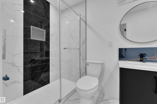 Contemporary bathroom featuring a glass-enclosed shower with white and black marble-look tiling, a built-in shower niche, a floating vanity with a white countertop, and a circular wall mirror - 16816 49 Street, Edmonton, AB 