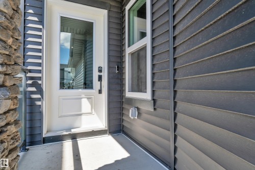 Entryway featuring a white door with an integrated glass panel, dark horizontal siding, and a partial stone facade - 16816 49 Street, Edmonton, AB 