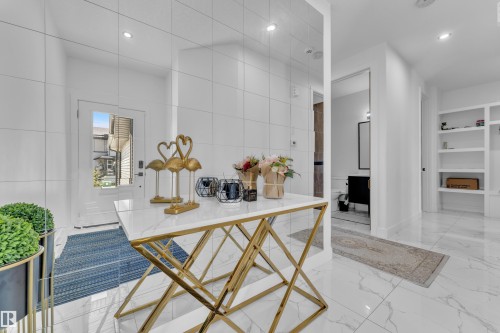 Bright entry foyer featuring large format white tile flooring, recessed lighting, a white paneled entry door with frosted glass, and built-in shelving - 16816 49 Street, Edmonton, AB 