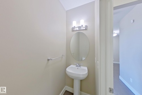 Pedestal sink with chrome faucet, an oval mirror, and wall-mounted vanity lighting - 4343 Crabapple Crescent, Edmonton, AB 