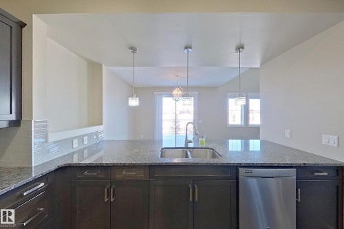 Kitchen island featuring a double basin stainless steel sink, granite countertop, and integrated dishwasher - 4343 Crabapple Crescent, Edmonton, AB 