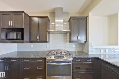 Kitchen featuring dark wood cabinetry, stainless steel appliances, granite countertops, and a white subway tile backsplash - 4343 Crabapple Crescent, Edmonton, AB 