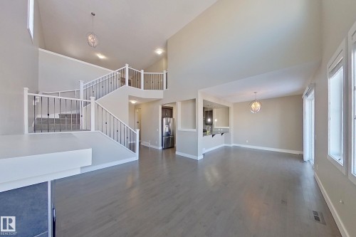 Vaulted ceilings define this open-concept space, featuring wood-finish flooring and a contemporary chandelier - 4343 Crabapple Crescent, Edmonton, AB 