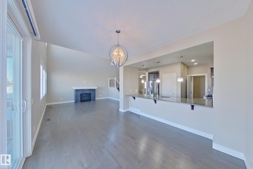 Vaulted ceiling living area featuring wood-finish flooring, a contemporary fireplace with a stone surround, and large sliding patio doors - 4343 Crabapple Crescent, Edmonton, AB 