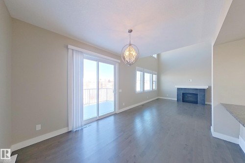 Spacious living area featuring wood-finish flooring, a contemporary chandelier, and a fireplace with a dark-tiled surround and white mantel - 4343 Crabapple Crescent, Edmonton, AB 