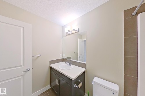 Bathroom featuring a single-door vanity with a white countertop and integrated sink, a rectangular mirror, and a three-bulb wall-mounted light fixture - 4343 Crabapple Crescent, Edmonton, AB 