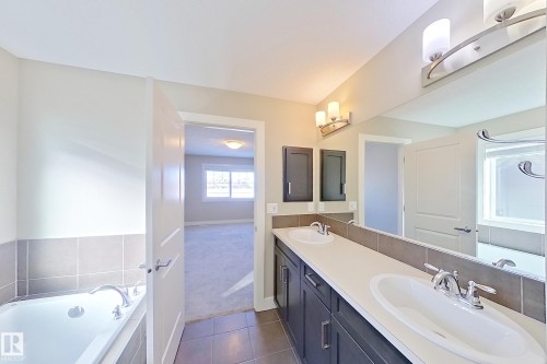 Bathroom featuring a dual vanity with undermount sinks, a built-in bathtub, tile wainscoting, and large format floor tiling - 4343 Crabapple Crescent, Edmonton, AB 