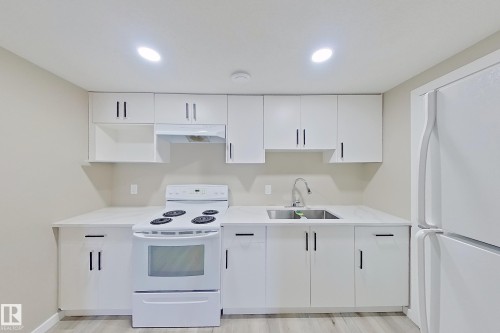 Kitchen featuring white cabinetry with dark hardware, a stainless steel double basin sink, white countertops, and a white electric range with an overhead vent - 4343 Crabapple Crescent, Edmonton, AB 