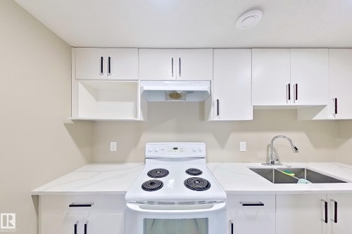 Modern kitchen featuring white cabinetry with black bar pulls, a white electric range, and light-toned countertops - 4343 Crabapple Crescent, Edmonton, AB 