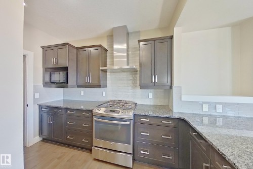 Contemporary kitchen featuring dark wood-finish cabinetry, stainless steel appliances, granite countertops, and a full-height tile backsplash - 4343 Crabapple Crescent, Edmonton, AB 