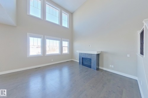 Vaulted ceiling space featuring wood-finish flooring, a contemporary fireplace with a stone surround, and multiple large windows - 4343 Crabapple Crescent, Edmonton, AB 