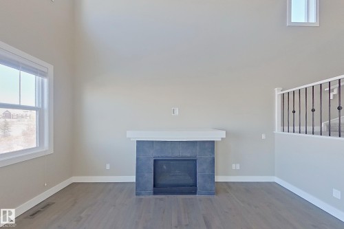 Two-story living area featuring a tile-surround fireplace with a white mantel, wood-finish flooring, and white trim - 4343 Crabapple Crescent, Edmonton, AB 