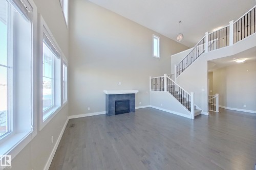 Two-story living area featuring a prominent staircase with black metal balusters, high ceilings, wood-finish flooring, and a fireplace with a dark tile surround and white mantel - 4343 Crabapple Crescent, Edmonton, AB 