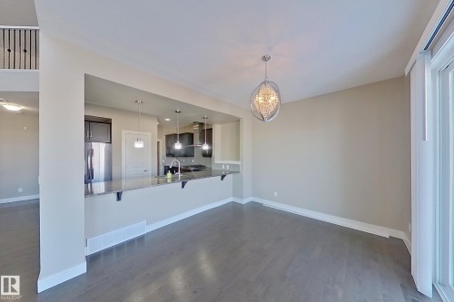 Open-concept dining area featuring wood-finish flooring, a contemporary chandelier, and direct access to the kitchen via a breakfast bar with pendant lighting - 4343 Crabapple Crescent, Edmonton, AB 