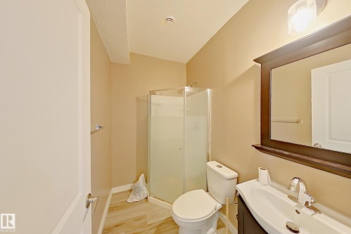 Bathroom featuring a glass-enclosed shower, wood-finish flooring, a contemporary vanity with a chrome faucet, and a framed mirror - 4343 Crabapple Crescent, Edmonton, AB 