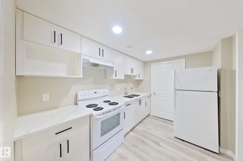 Galley kitchen featuring white cabinetry with dark hardware, white countertops, a four-burner electric range, and a white refrigerator - 4343 Crabapple Crescent, Edmonton, AB 