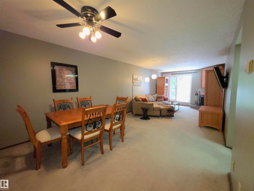 Open-concept living space featuring neutral carpet flooring, a ceiling fan with integrated lighting, and a sliding glass door leading to exterior - 302 10335 118 Street, Edmonton, AB 