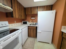 Compact kitchen featuring wood-finish cabinetry, white countertops, and white appliances including a refrigerator, dishwasher, and electric range with an overhead microwave - 