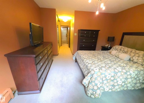 Carpeted bedroom featuring an attached full bathroom with a tub/shower combination, and a built-in closet with mirrored sliding doors - 302 10335 118 Street, Edmonton, AB 