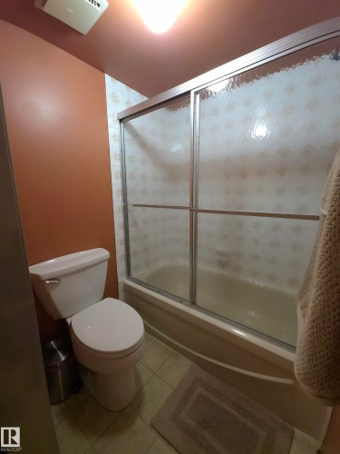 Bathroom featuring a bathtub with frosted sliding glass doors, white toilet, and tiled flooring - 302 10335 118 Street, Edmonton, AB 