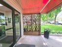 Inviting entryway featuring a red awning, decorative tree-patterned screen, light-colored siding, concrete flooring, and a large glass entry door - 302 10335 118 Street, Edmonton, AB 