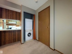 Stacked washer and dryer unit, wood-finish cabinetry with open shelving, and light tone carpeting - 