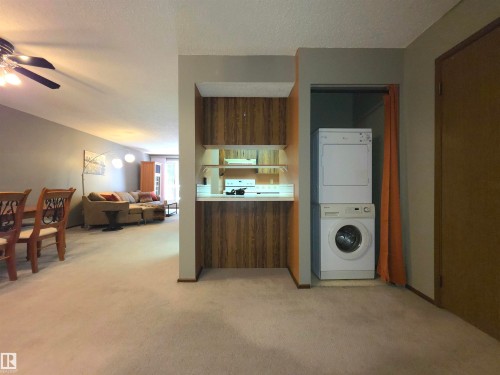 Laundry nook featuring a stacked washer and dryer, complemented by a kitchen pass-through with wood-finish paneling and shelving - 302 10335 118 Street, Edmonton, AB 