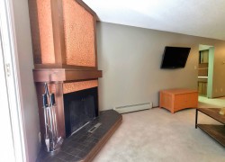 Corner fireplace with a wood mantel, textured copper-toned surround, and a dark tile hearth - 