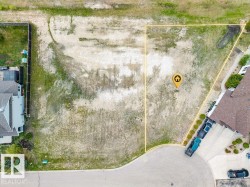 Vacant lot with defined property lines, featuring partial landscaping with grass and shrubs, and direct access to a paved street - 