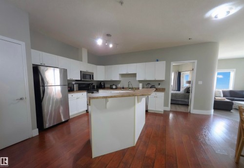 Kitchen featuring wood-finish flooring, white cabinetry, light-toned countertops, stainless steel appliances, and an island with a breakfast bar - 104 4312 139 Avenue, Edmonton, AB 